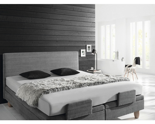 Schlafzimmer mit Boxspringbett, Nachttischlampe und Badewanne im Hintergrund