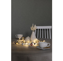 Décoration avec guirlande lumineuse, pomme de pin, vase et tasses sur une table