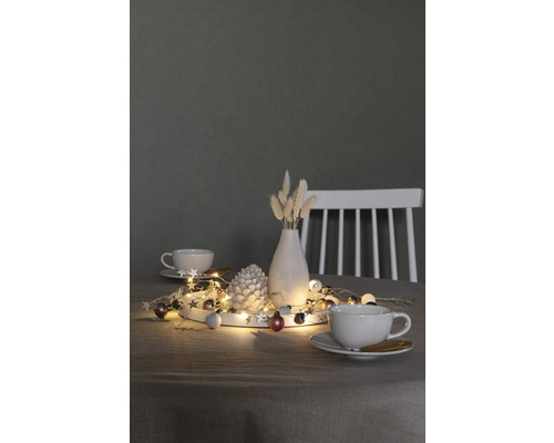 Décoration avec guirlande lumineuse, pomme de pin, vase et tasses sur une table