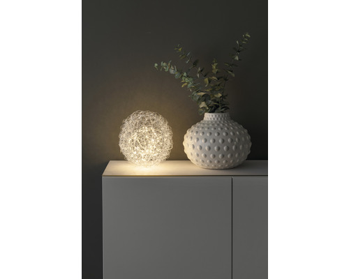 Dekorative Kugel-Tischleuchte neben einer Vase mit Pflanzen auf einem Schrank