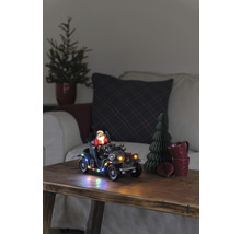 Scène de Noël décorative avec le Père Noël dans une voiture ancienne, éclairée, sur une table en bois.