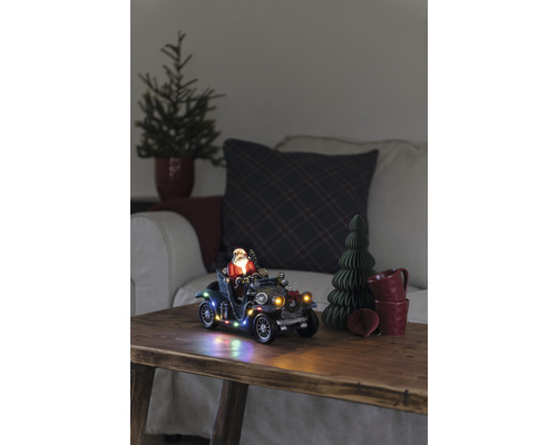 Scène de Noël décorative avec le Père Noël dans une voiture ancienne, éclairée, sur une table en bois.