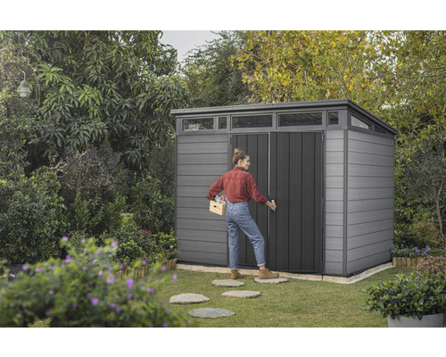 Gartenszene mit Gerätehaus und Frau, die eine Kiste trägt