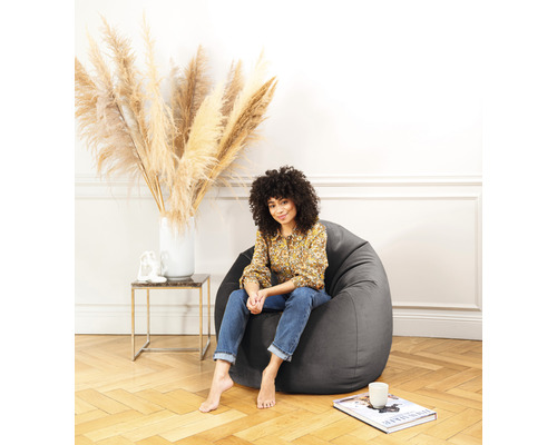 Femme assise dans un pouf gris dans une pièce lumineuse.