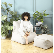 Femme assise sur un pouf de couleur claire avec un tabouret assorti dans une pièce avec des plantes d''intérieur
