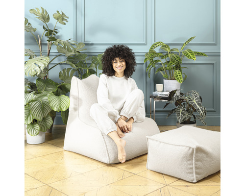 Femme assise sur un pouf de couleur claire avec un tabouret assorti dans une pièce avec des plantes d''intérieur
