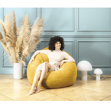 Une femme est assise dans un pouf jaune dans une pièce lumineuse.