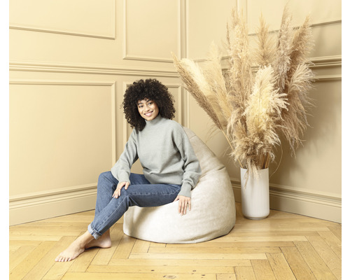 Femme assise sur un pouf clair dans une pièce avec des fleurs séchées dans un vase.