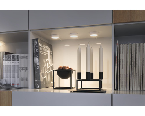 Dekoratives Regal mit Unterbauleuchten, Büchern, Kerzen und einer Schale mit Inhalt