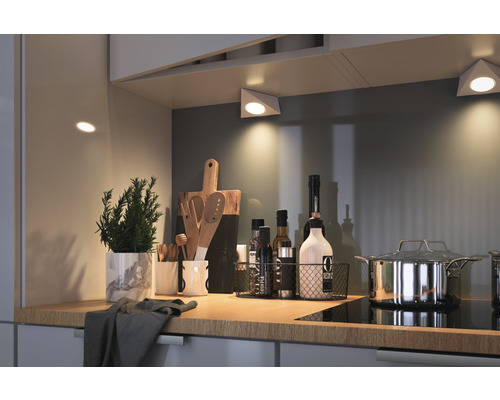 Scène de cuisine avec éclairage sous armoire, herbes, ustensiles de cuisine et casserole sur un plan de travail