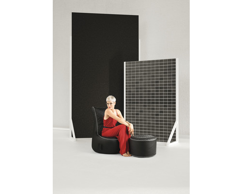 Frau sitzt auf einem schwarzen Sessel mit Fusshocker vor dekorativen Paneelen