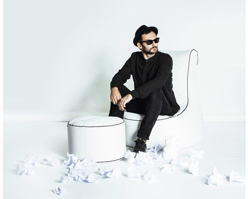 Mann sitzt auf Sessel mit Hocker inmitten zerknülltem Papier