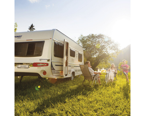 Familie entspannt sich vor einem Wohnwagen auf einer Wiese.