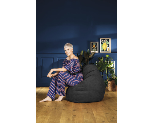 Frau sitzt auf einem schwarzen Sitzsack in einem Wohnzimmer mit Pflanzen und Wandkunst