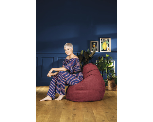 Femme assise sur un pouf bordeaux dans le salon devant un mur bleu avec décoration