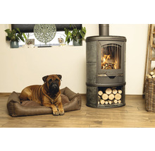 Bullmastiff liegt in einem Hundebett neben einem Kaminofen mit Holzfach