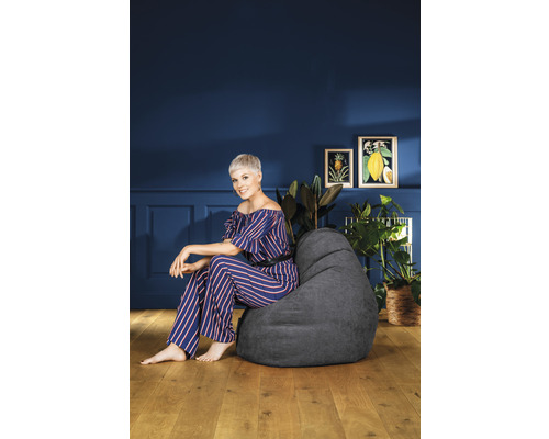 Femme assise sur un pouf gris dans un salon avec des plantes et des tableaux