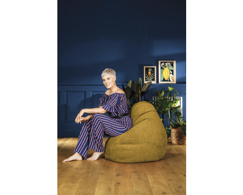 Femme assise sur un pouf poire vert dans une pièce avec décoration