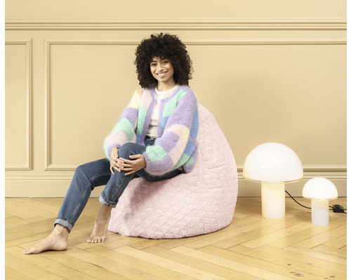 Une femme est assise sur un pouf rose à côté de deux lampes champignons.