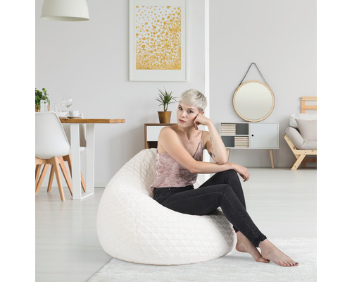 Une femme est assise sur un pouf blanc dans un salon lumineux.