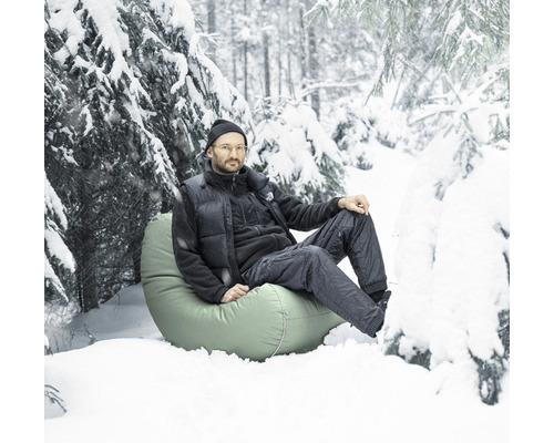 Mann sitzt auf einem Sitzsack im Schnee in einer verschneiten Waldlandschaft.