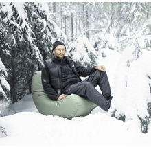 Mann sitzt auf einem Sitzsack im Schnee in einer Waldlandschaft.