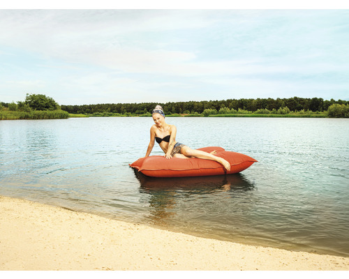 Femme se détend sur un coussin flottant rouge sur un lac.