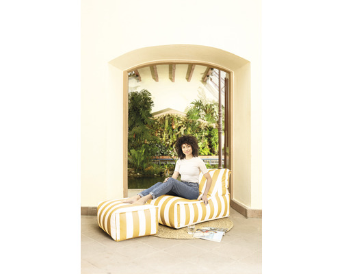 Femme assise dans une pièce sur un pouf rayé avec repose-pieds