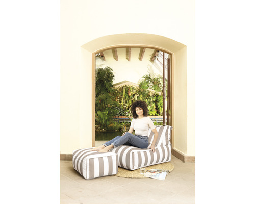 Frau sitzt auf einem gestreiften Lounge-Sessel mit Hocker im Garten