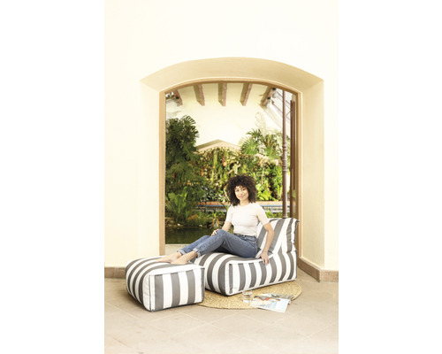 Femme assise sur un pouf rayé avec repose-pieds devant un bassin de jardin