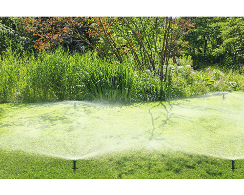 Rasensprenger bewässern einen grünen Rasen in einem Garten.