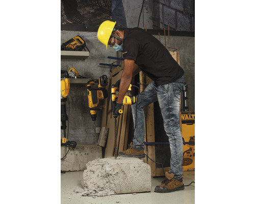 Un ouvrier portant un casque de sécurité utilise un marteau perforateur pour travailler un morceau de béton.