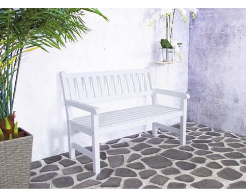 Banc de jardin blanc sur sol en pierre devant un mur