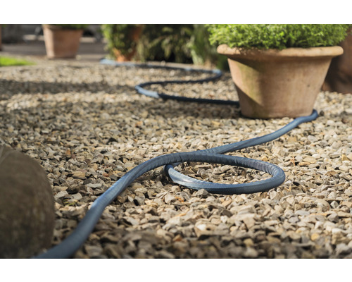 Scène de jardin avec tuyau textile flexible sur chemin de gravier à côté de pots de fleurs