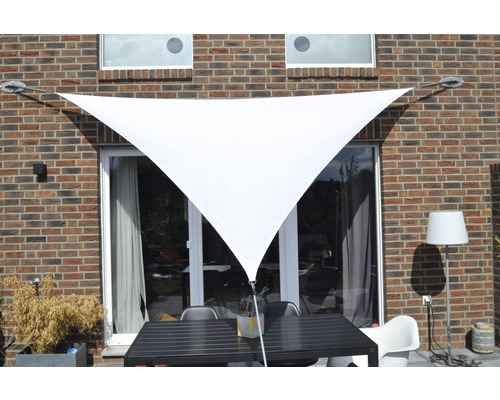Voile d''ombrage triangulaire devant un mur de maison avec mobilier de terrasse