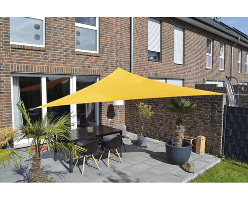 Voile d''ombrage triangulaire jaune au-dessus d''une terrasse avec table et chaises devant une maison d''habitation.