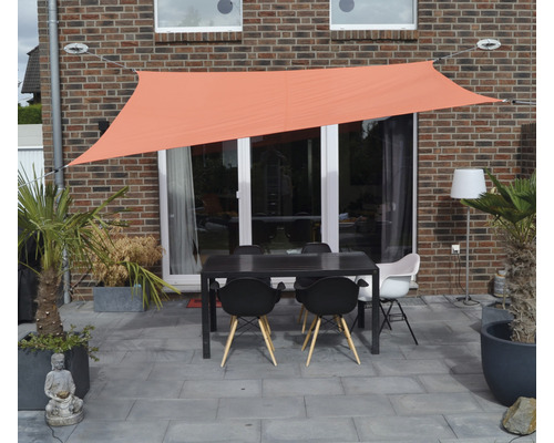Terrasse avec voile d''ombrage, table et chaises devant un mur de maison
