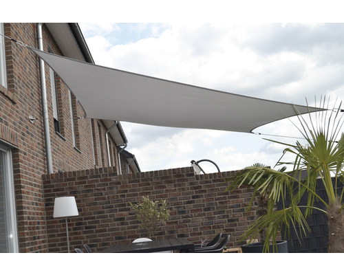 Voile d''ombrage triangulaire au-dessus d''une terrasse avec mur de briques et mobilier de jardin
