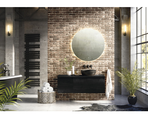 Salle de bains moderne avec baignoire îlot, sèche-serviettes, meuble sous-lavabo, miroir rond avec éclairage et mur en briques