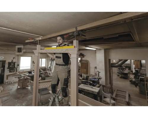 Ein Handwerker montiert einen Holzrahmen mit einer Wasserwaage in einer Werkstatt.