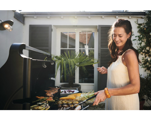 Une femme fait griller des légumes et de la viande sur un barbecue à l''extérieur.