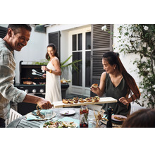 Scène d''un groupe de personnes faisant un barbecue à l''extérieur, avec de la nourriture sur la table et un barbecue en arrière-plan.