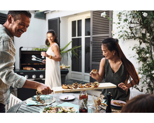 Scène d''un groupe de personnes faisant un barbecue à l''extérieur, avec de la nourriture sur la table et un barbecue en arrière-plan.