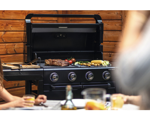 Barbecue à gaz noir avec des grillades et des personnes au premier plan