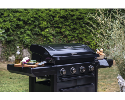 Barbecue à gaz noir avec quatre brûleurs et légumes sur une planche en bois