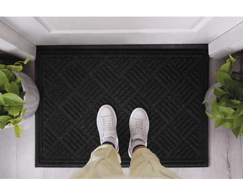 Schwarze Fußmatte mit geometrischem Muster vor einer Tür
