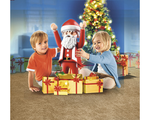 Deux enfants avec une figurine de Noël Playmobil et des cadeaux devant un sapin de Noël.