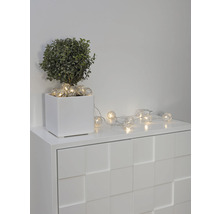 Guirlande lumineuse décorative avec des lampes sphériques sur une commode blanche à côté d''une plante en pot.