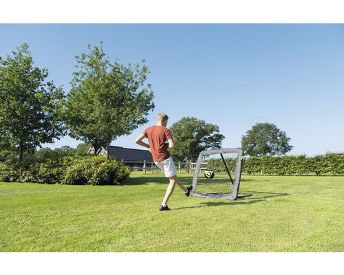 Junge schiesst Fussball in ein tragbares Fussballtor im Garten.
