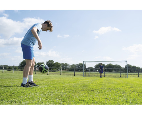Adolescent jonglant avec un ballon de foot sur un terrain de football.